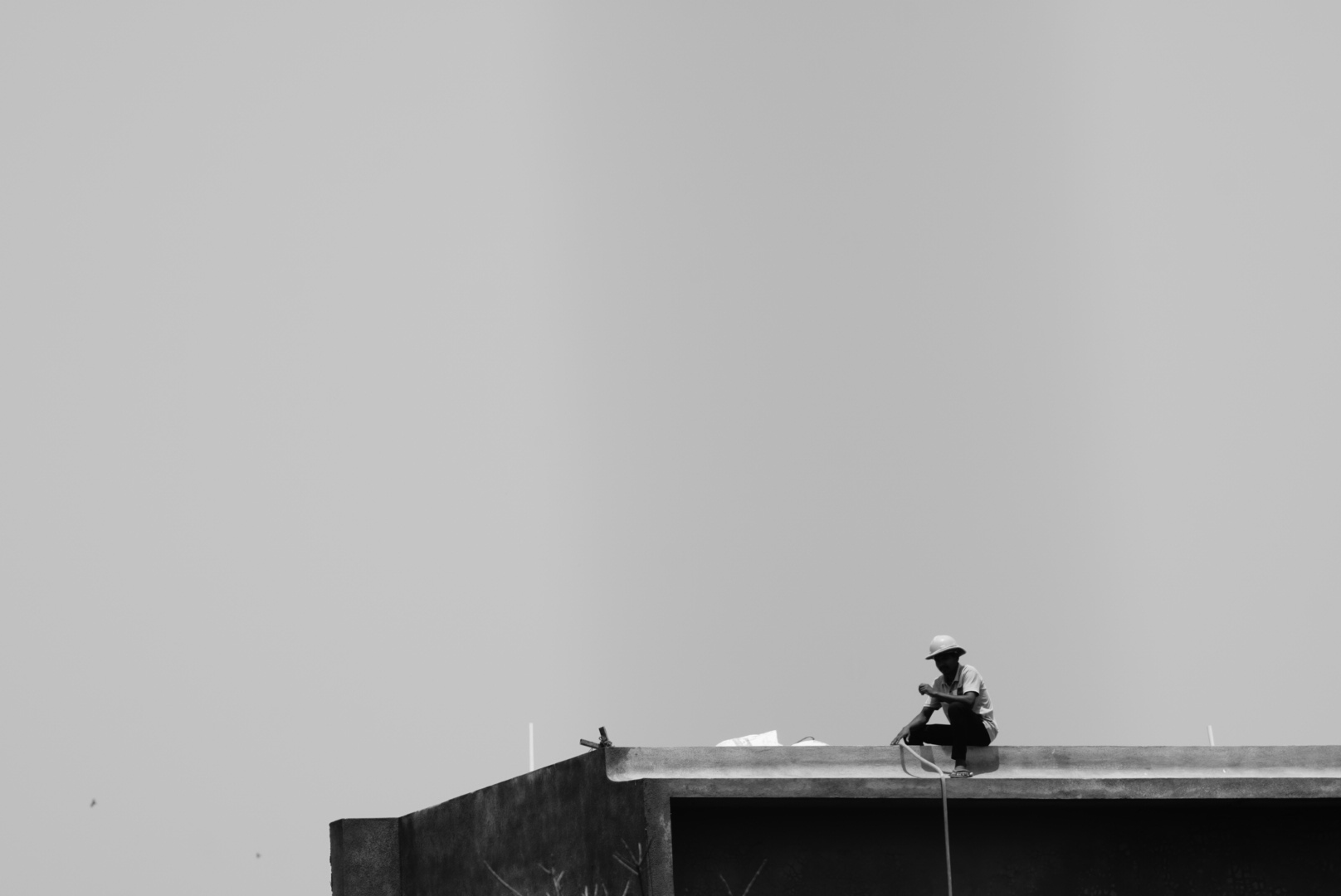 A worker sitting on the edge of a rooftop against an empty grey sky