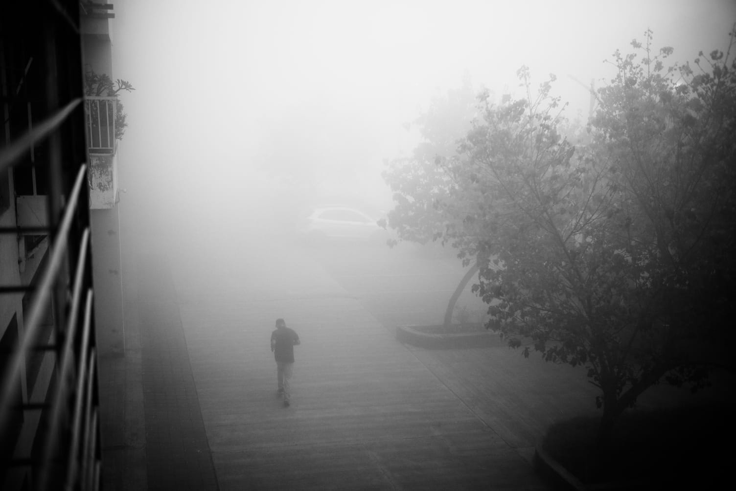 A lone runner on a path in dense fog, seen from a balcony above