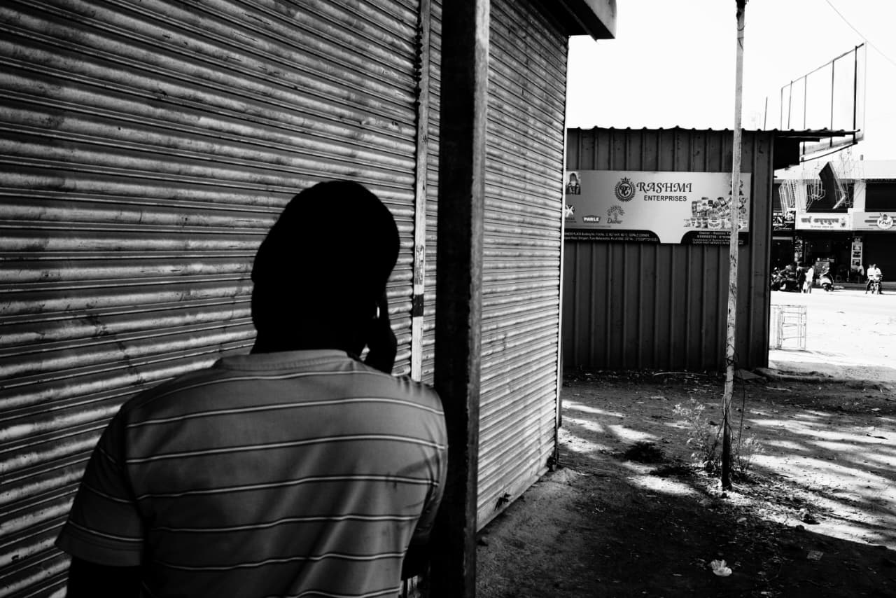 A man in a striped shirt on the phone, turned away, beside a shuttered storefront