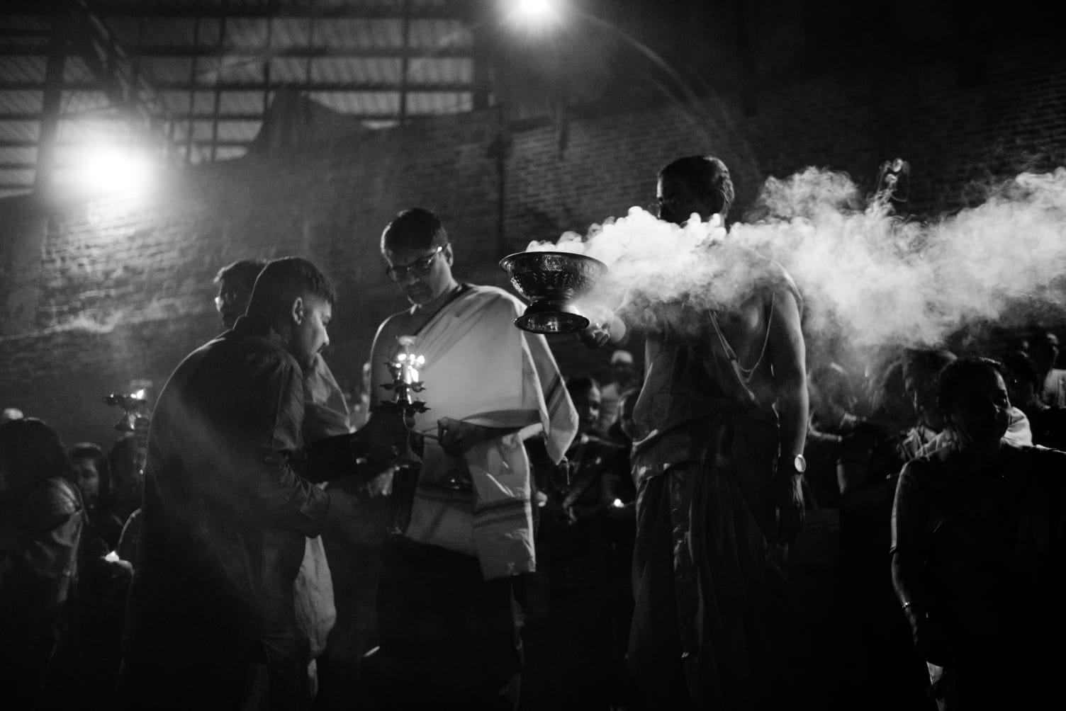 Men performing an evening aarti, incense smoke lit from behind