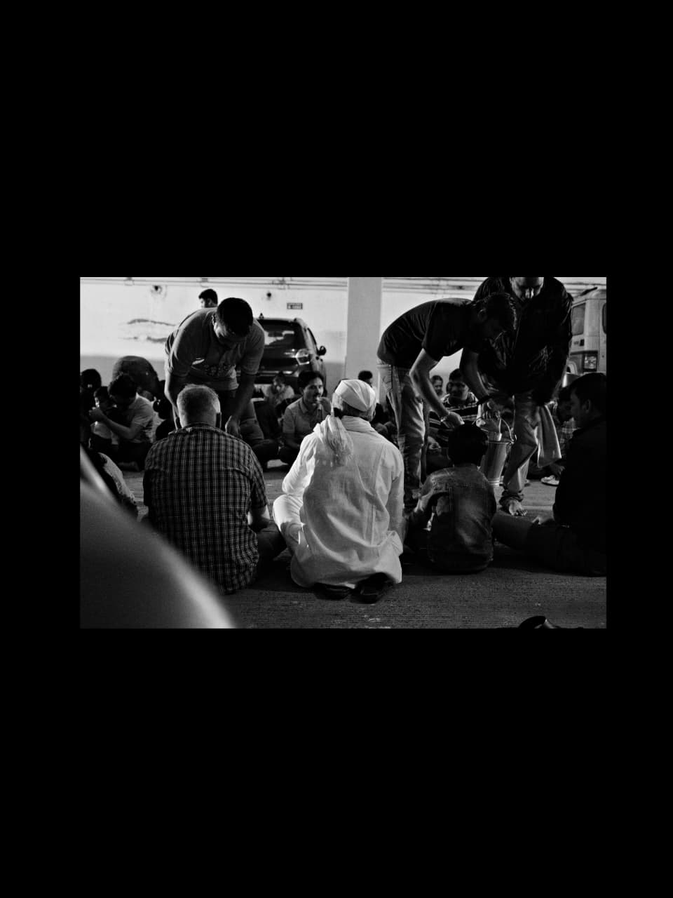 A crowd seated on the ground being served, men moving between the rows